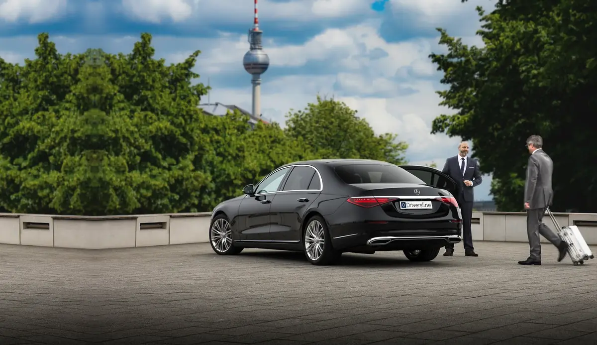 Chauffeur an der geöffneten Fondtür einer schwarzen Mercedes-Benz S-Klasse, im Hintergrund der Berliner Fernsehturm