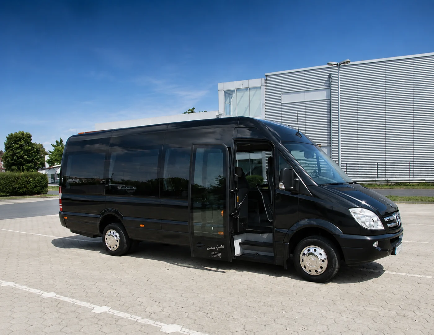 A black Mercedes-Benz Sprinter as a minibus with its door open on a forecourt