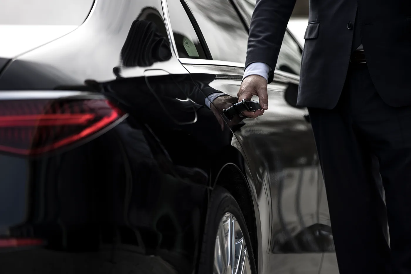 Chauffeur in a suit opening the door handle of a black sedan
