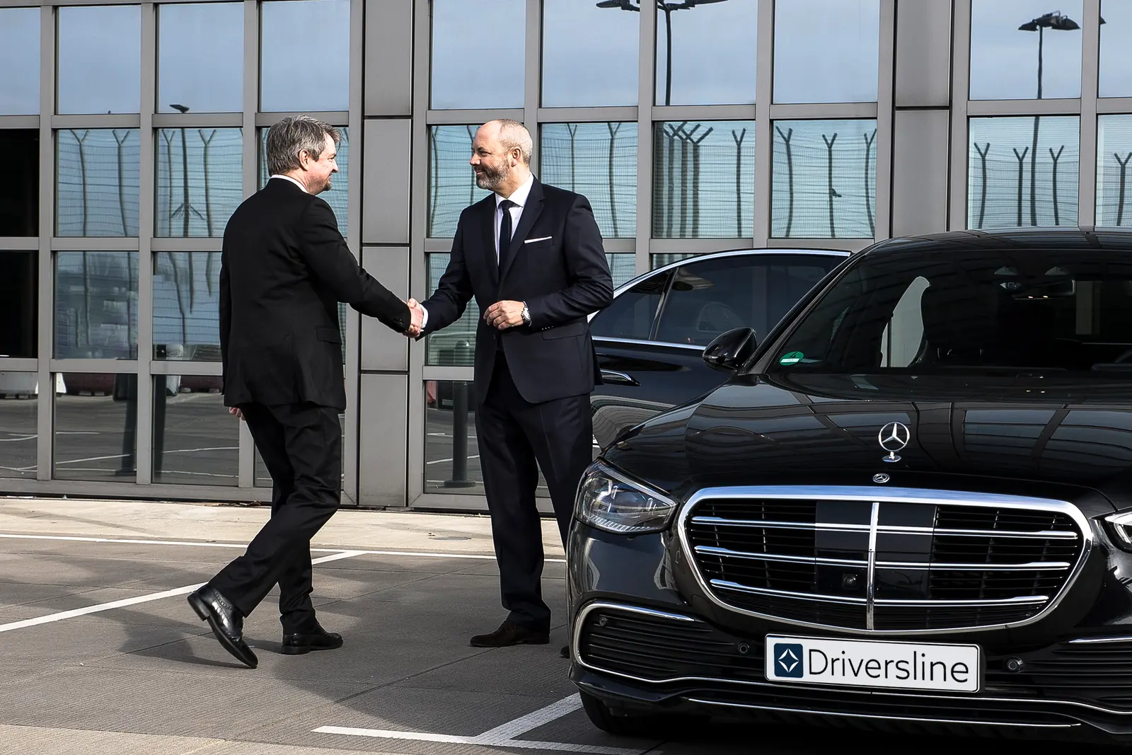 Chauffeur in a suit greeting a guest with a handshake beside a black sedan