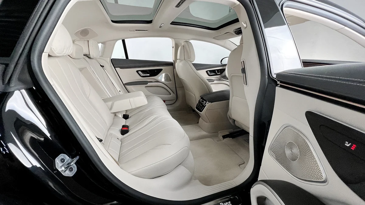 The open rear door of a sedan, showing light leather seats and a panoramic roof