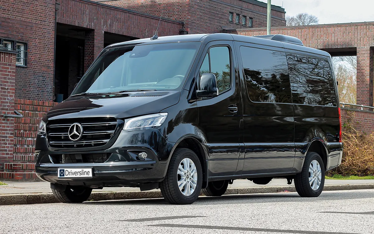 Black Driversline Mercedes-Benz Sprinter minibus at an angle from the front in front of a brick facade