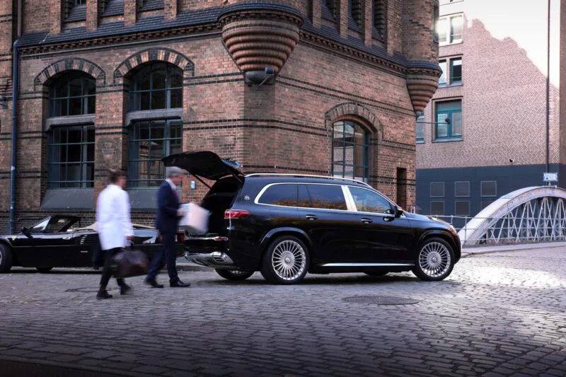 Chauffeur and guest at the open tailgate of a black Mercedes-Maybach GLS on cobblestones in Hamburg's Speicherstadt, luggage being loaded