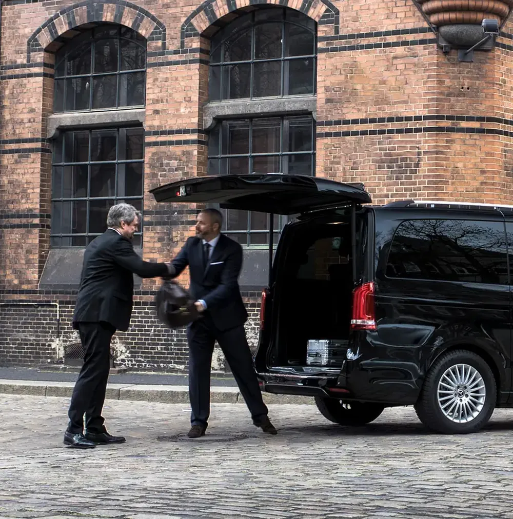 Chauffeur taking a passenger's luggage at the open tailgate of a black V-Class