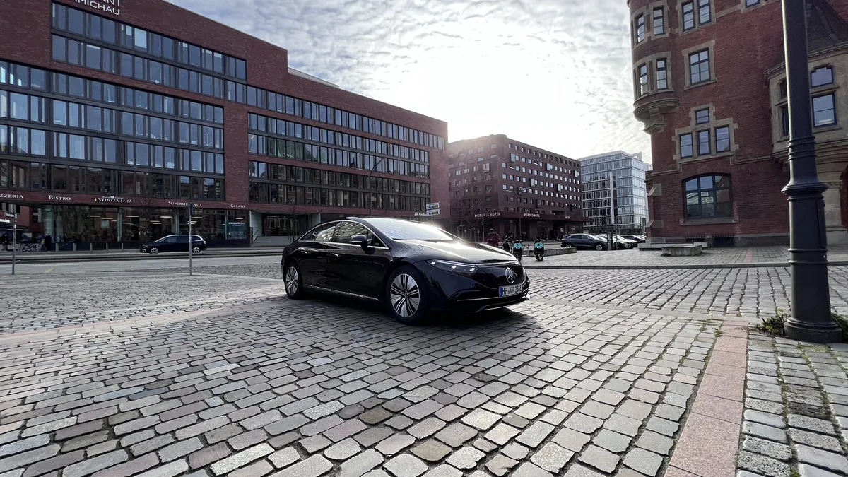 A black Mercedes-Benz EQS sedan on cobblestones in front of office buildings in Hamburg's HafenCity
