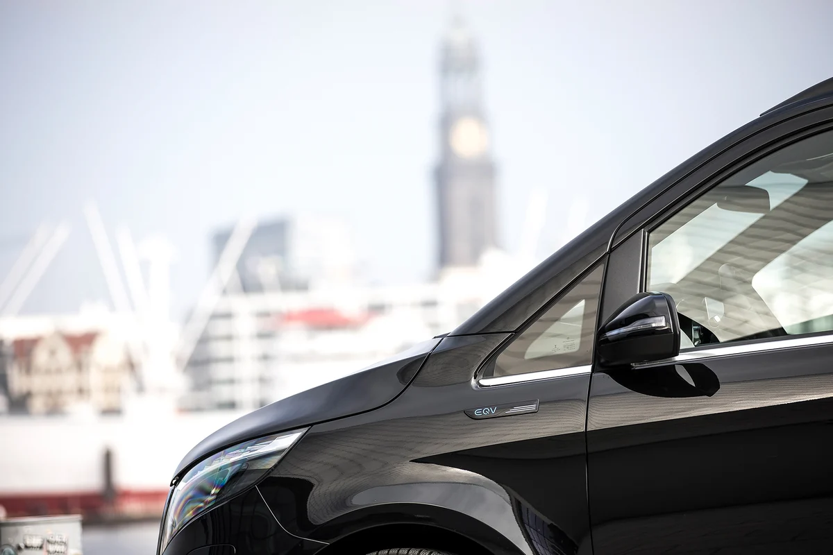 The front of a black electric Mercedes-Benz van, the tower of Hamburg's Michel church behind