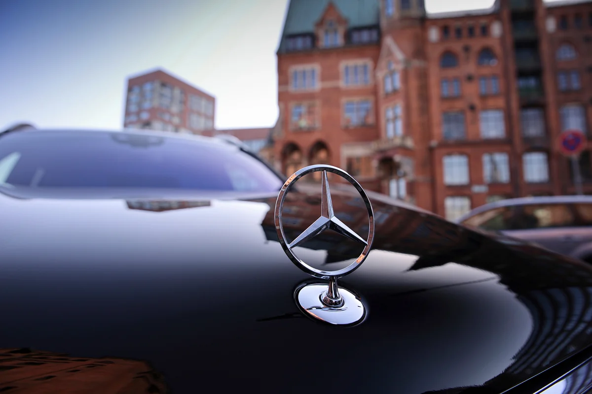 The Mercedes star on the bonnet of a black sedan, with the brick facades of Hamburg's Speicherstadt behind
