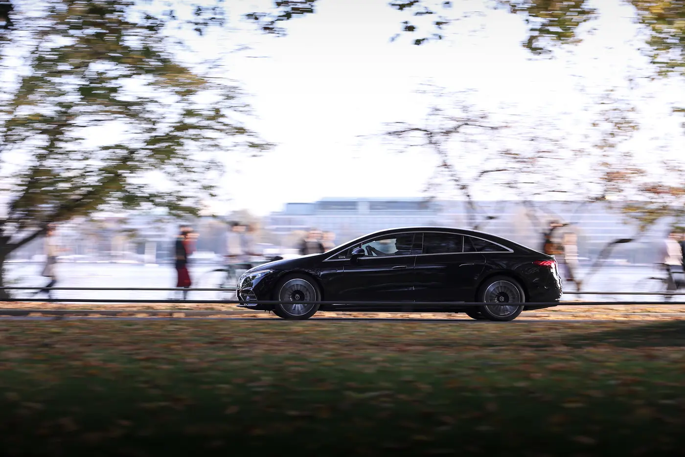 Schwarze Limousine in voller Fahrt von der Seite, unter herbstlichen Bäumen