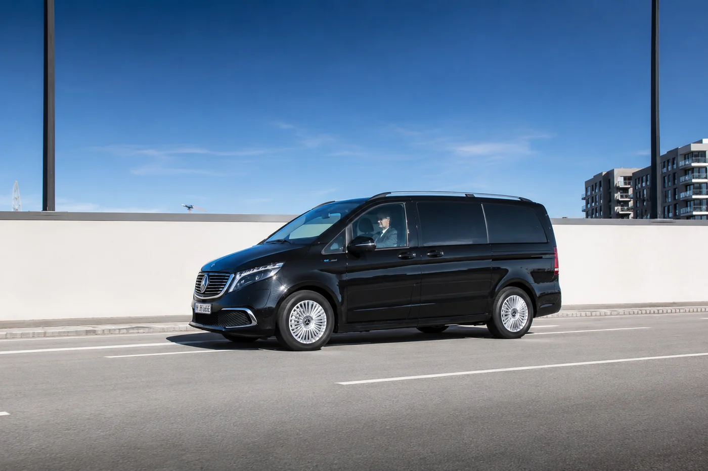 A black Mercedes-Benz van with the driver at the wheel, on the move along a road