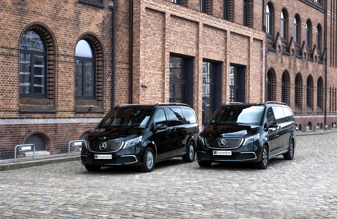 Two black Mercedes-Benz vans side by side on cobblestones in front of a brick facade