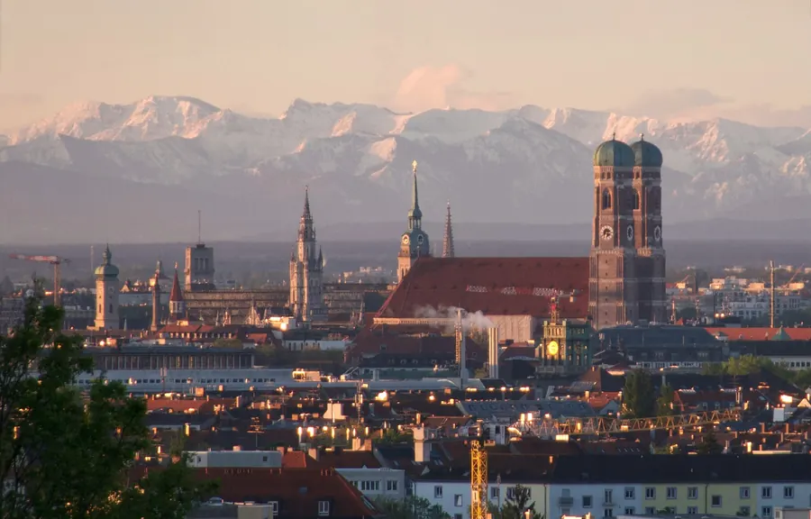 Münchner Altstadt mit der Frauenkirche, dahinter die verschneiten Alpen im Abendlicht