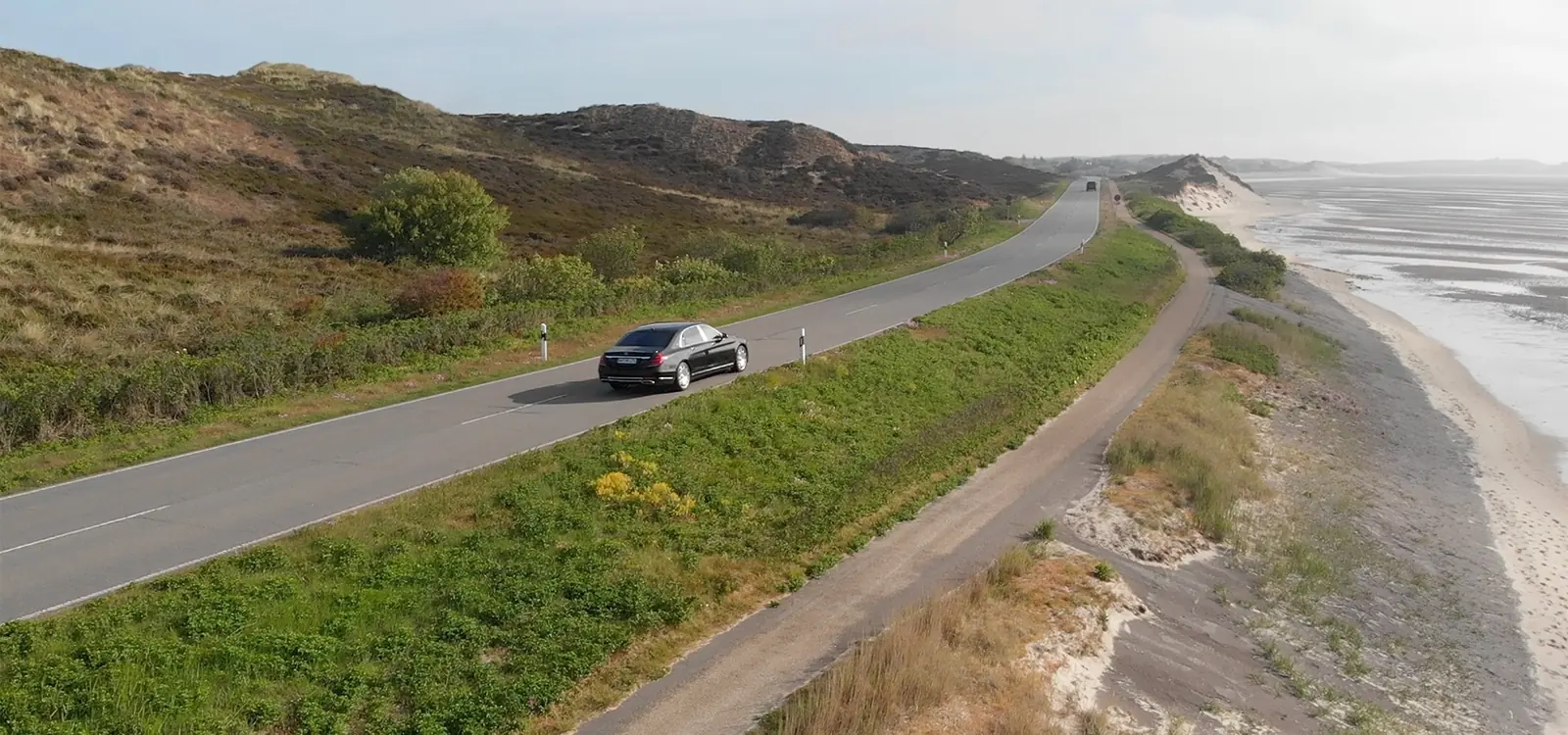 A sedan on the move along the coast road between the dunes on Sylt, seen from the air
